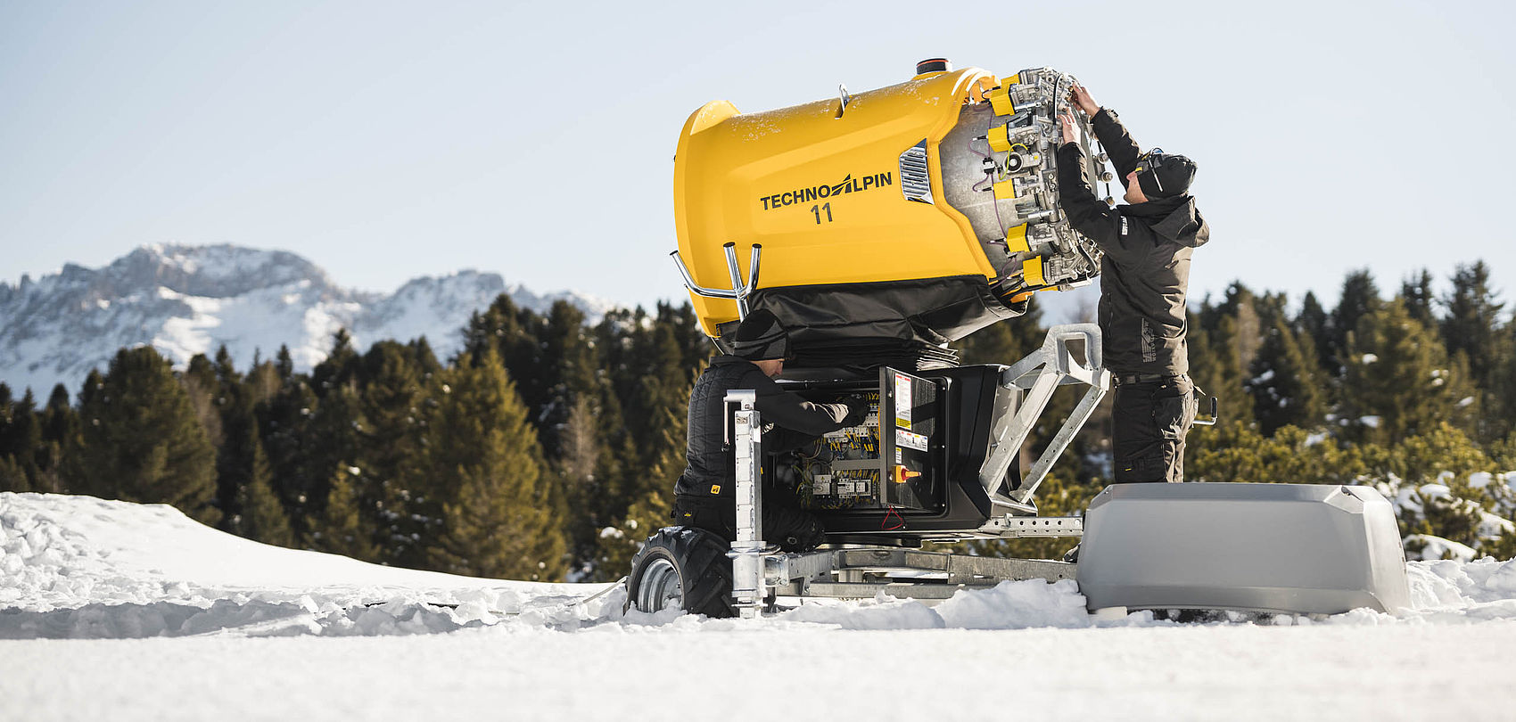 Technicien travaille sur canon à neige TechnoAlpin jaune dans la neige
