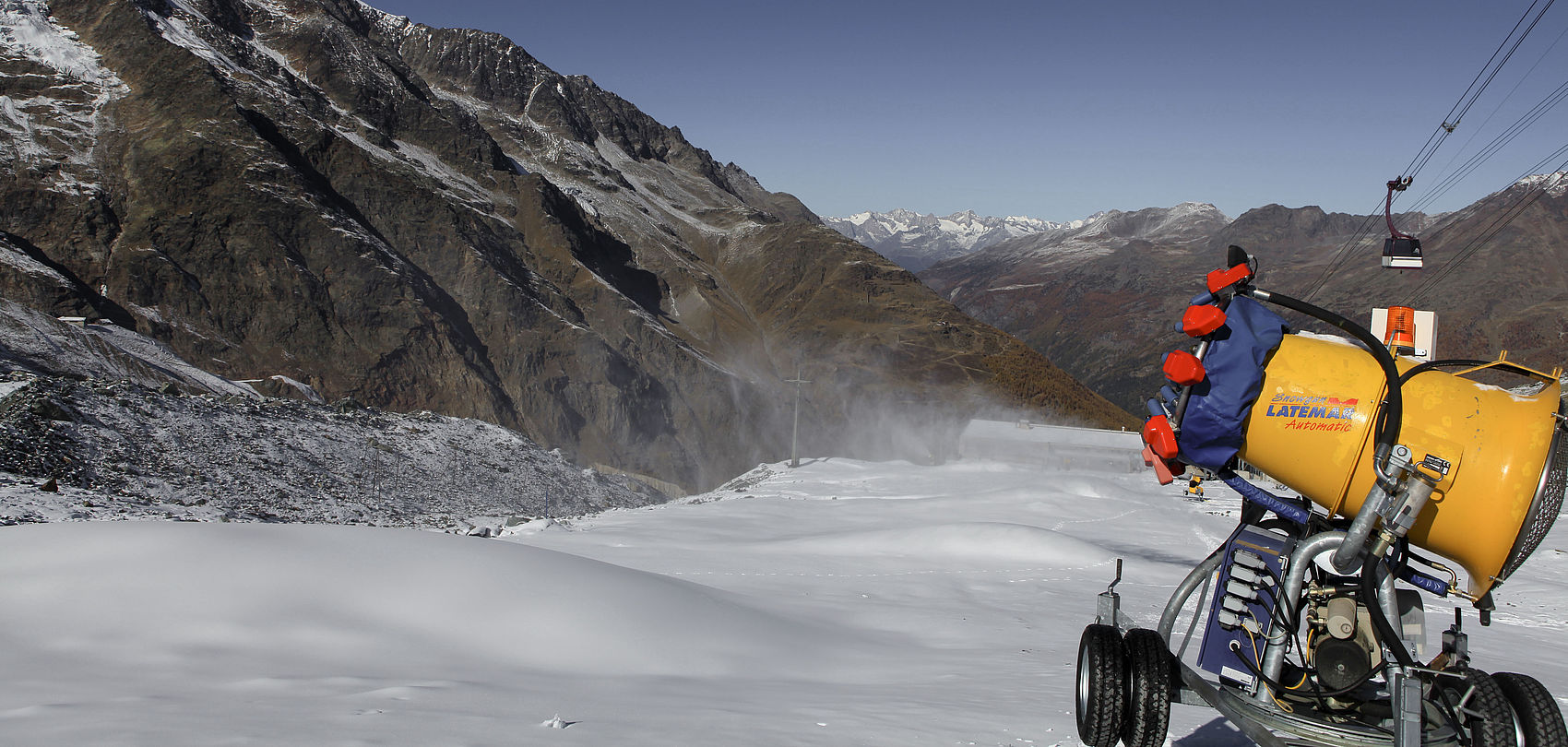 Yellow fan gun M90 on trailer in high alpine terrain with ski slope and chairlift