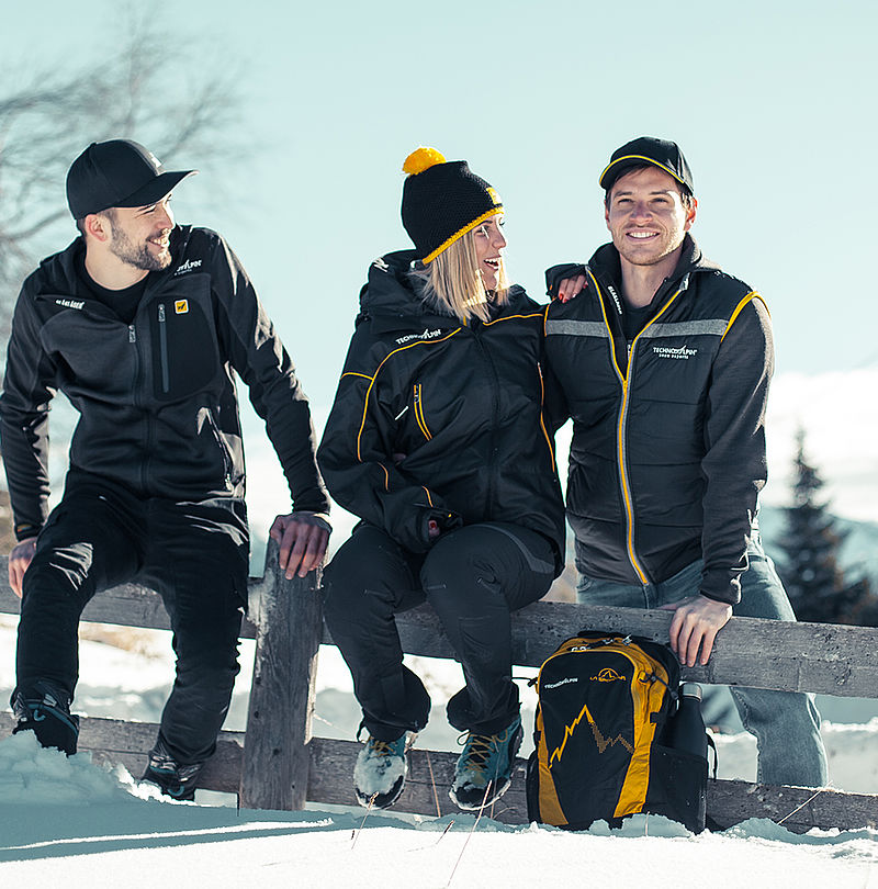 Trois personnes en vêtements TechnoAlpin assises sur clôture en bois dans la neige