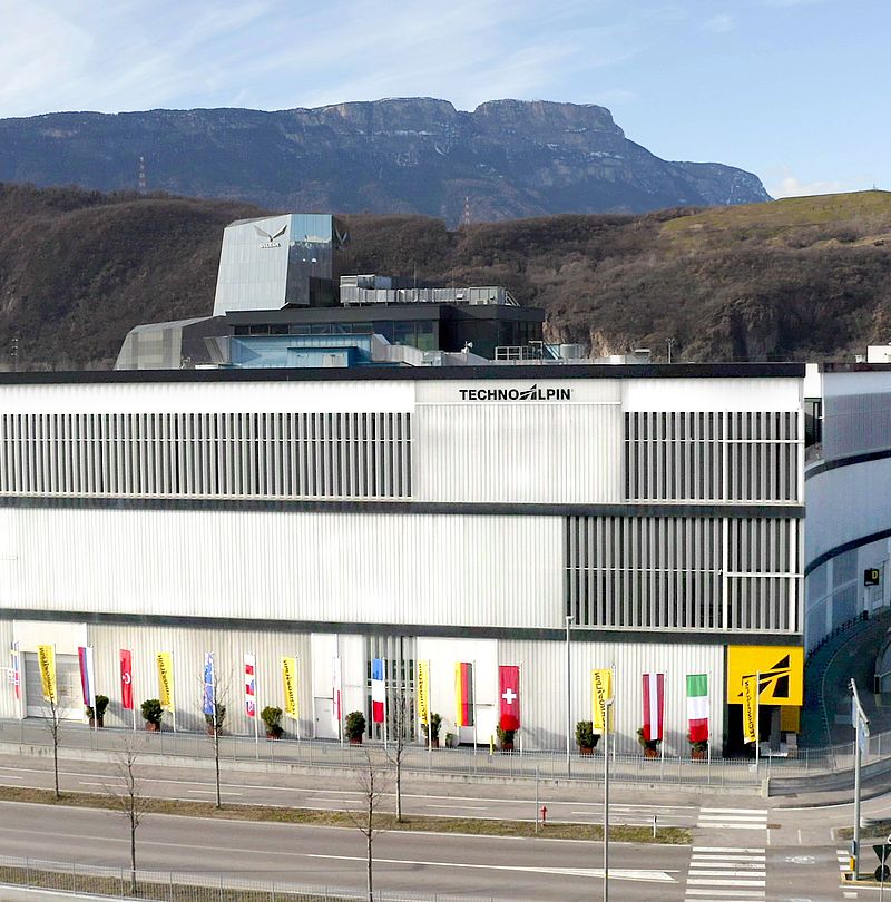 TechnoAlpin Firmengebäude in Bozen mit beflaggtem Eingang vor Bergkulisse Südtirol