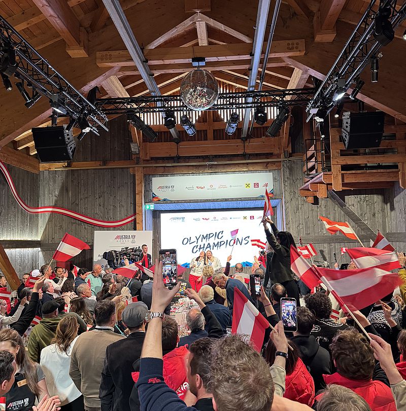 Cheering crowd with Austrian flags at Austria House celebrates Olympic champions on stage