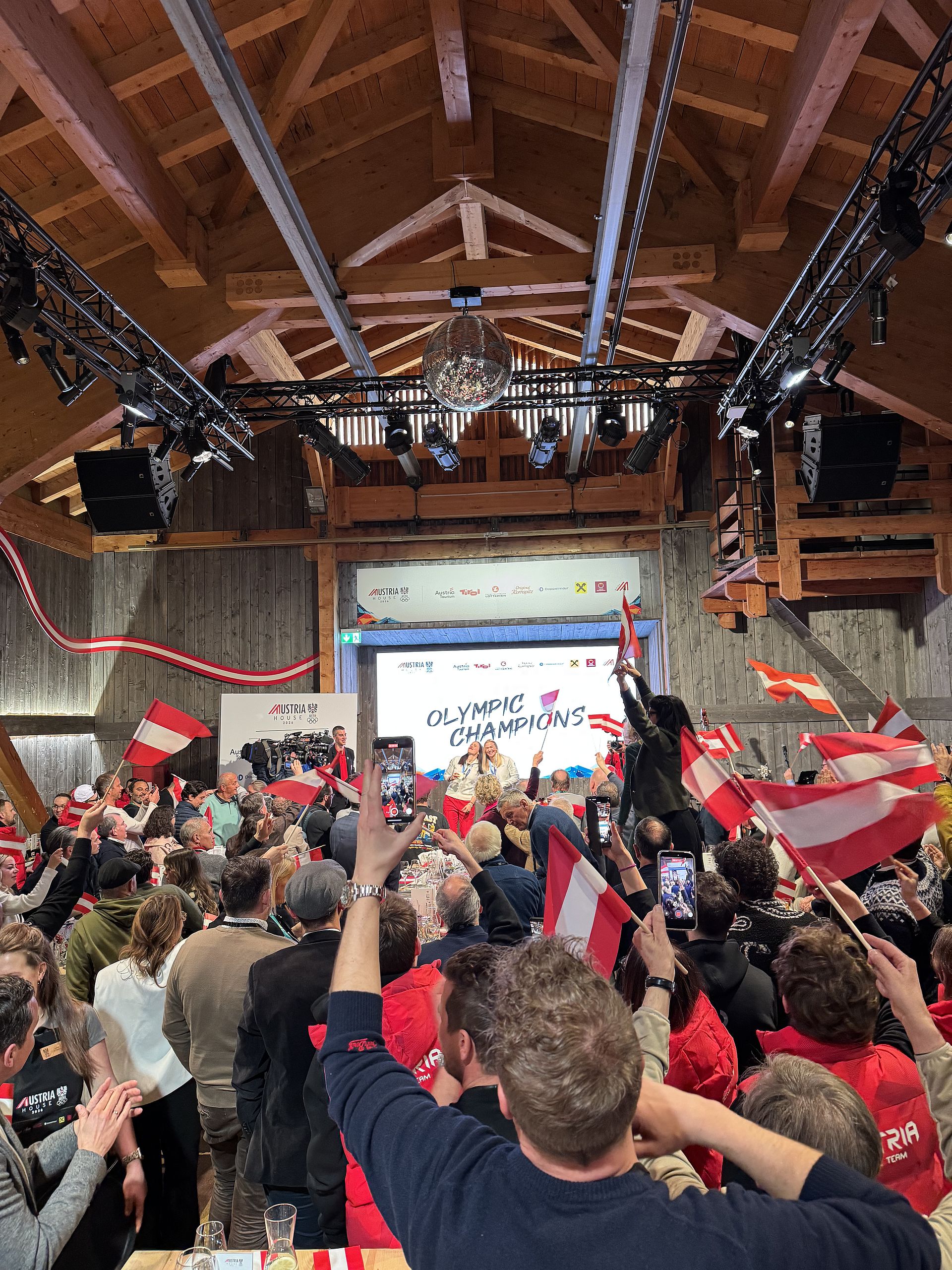Cheering crowd with Austrian flags at Austria House celebrates Olympic champions on stage