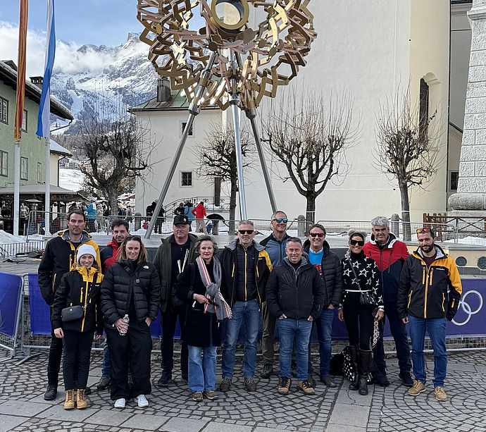 Group photo in front of golden snowflake sculpture in church square in Cortina at Olympics