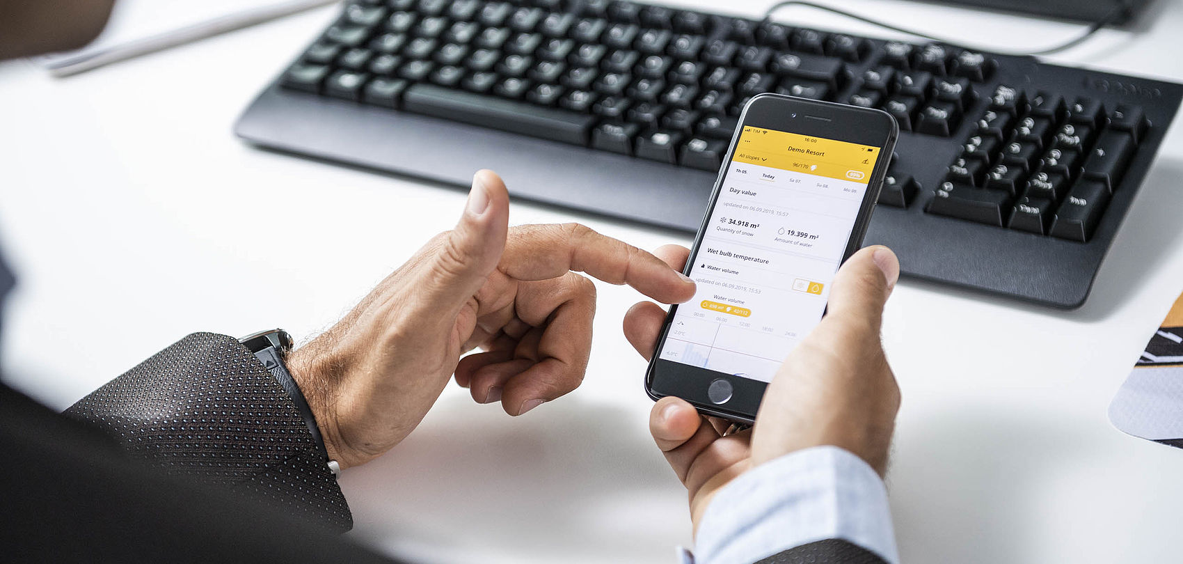 Mains utilisant l'application TechnoAlpin Snowmaster sur smartphone au bureau