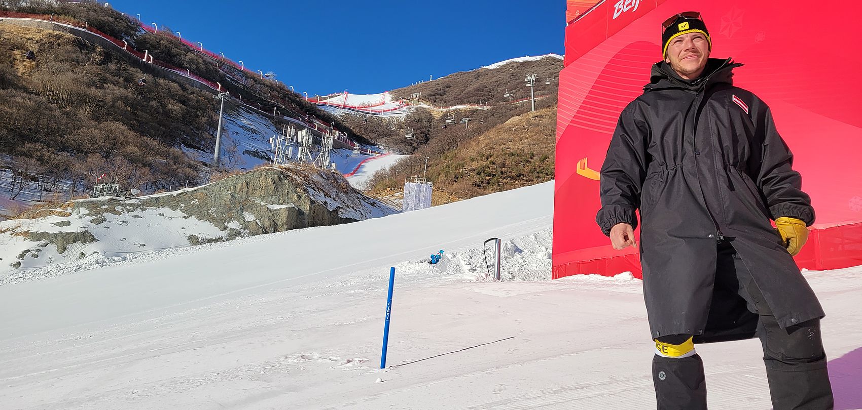 Employé avec bonnet TechnoAlpin devant la zone d'arrivée des JO de Pékin pour ski alpin.