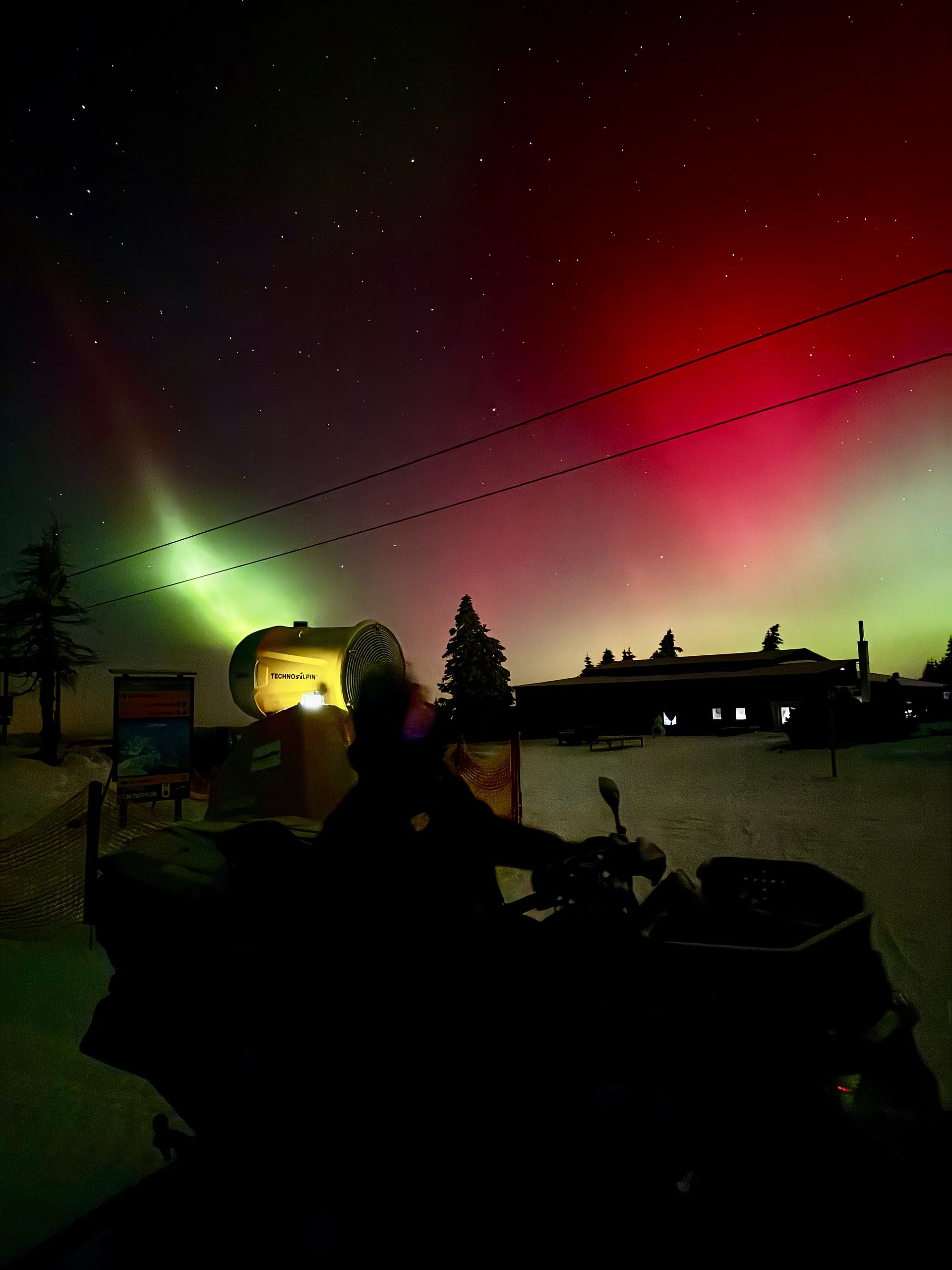 Schneekanone unter rot-grünen Polarlichtern am Sternenhimmel mit Quad-Silhouette