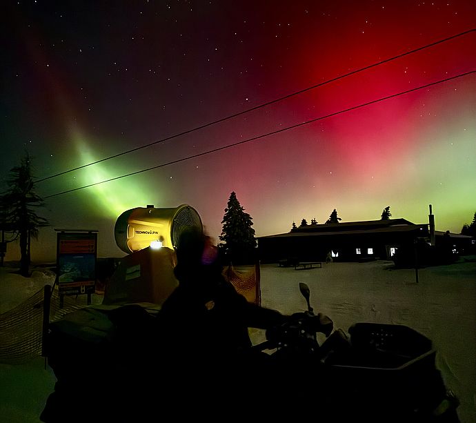 Schneekanone unter rot-grünen Polarlichtern am Sternenhimmel mit Quad-Silhouette
