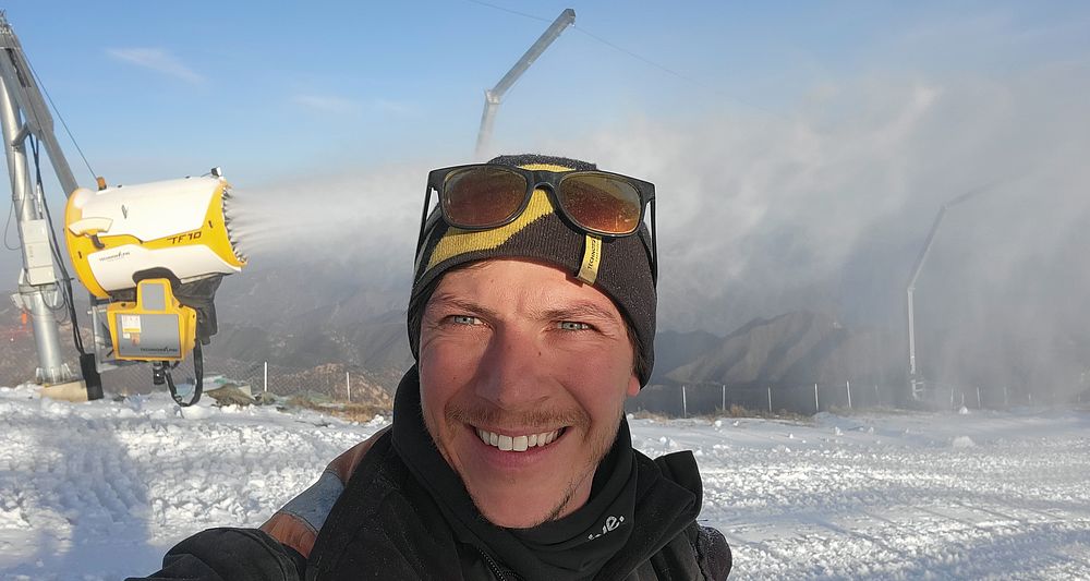 Lächelnder Mann mit Mütze und Sonnenbrille macht Selfie im Schnee neben gelbem TF10-Schneeerzeuger.