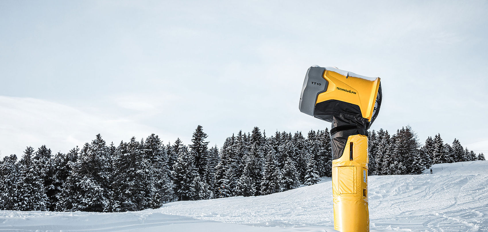 TechnoAlpin TT10 snow generator on snowy slope in front of snow-covered coniferous forest