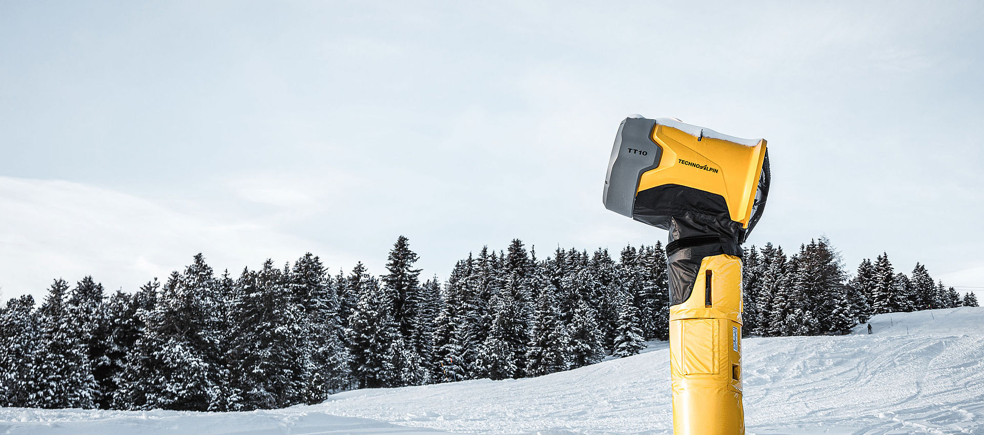 Generatore di neve TechnoAlpin TT10 su pista innevata davanti a foresta di conifere