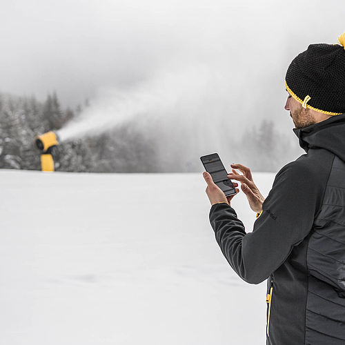 Bediener nutzt Smartphone-App neben TechnoAlpin Schneekanone im Skigebiet