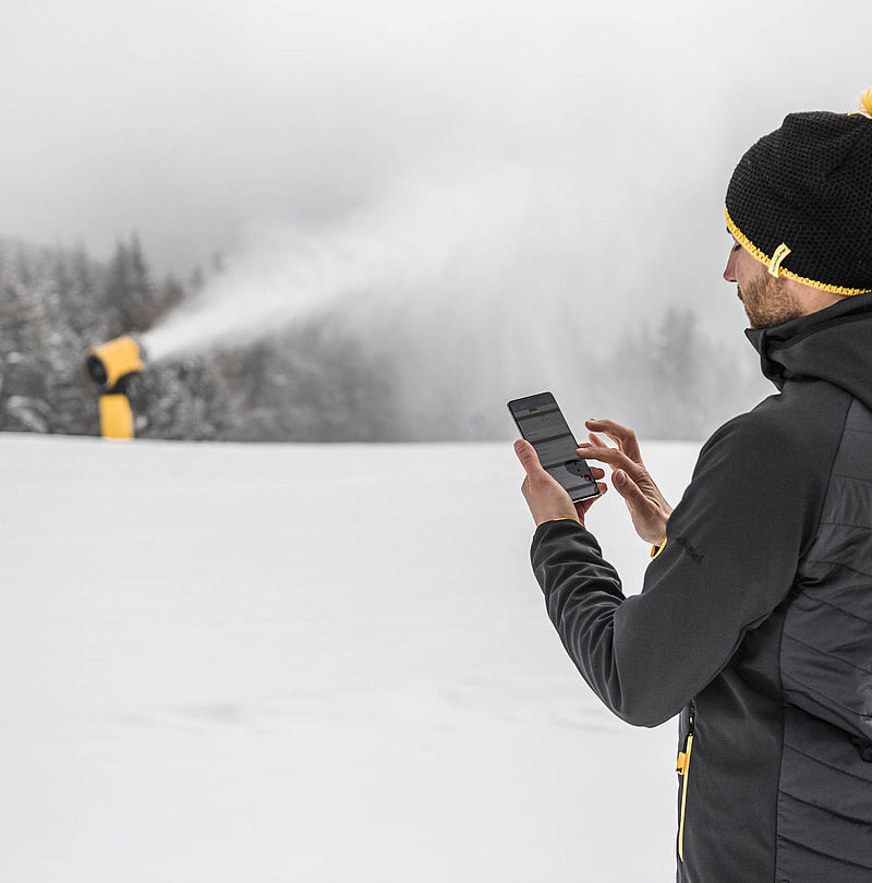 Operator uses smartphone app next to TechnoAlpin snow gun on the ski slope