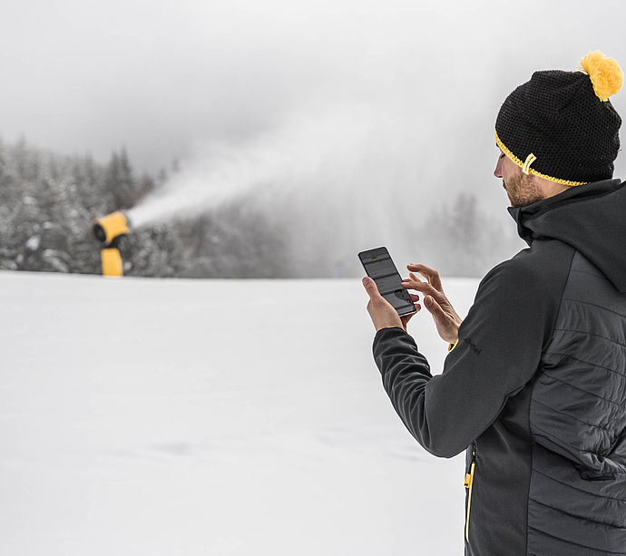 Bediener nutzt Smartphone-App neben TechnoAlpin Schneekanone im Skigebiet