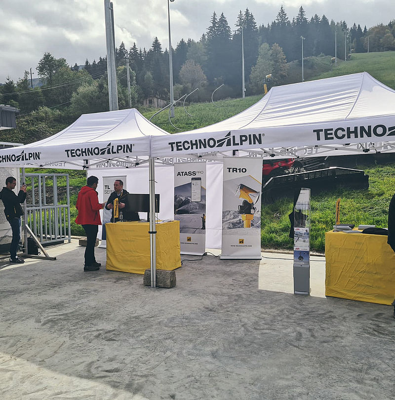 TechnoAlpin exhibition booth with white tents and ATASS Pro, TR10, TL Series banners at Romanian ski resort