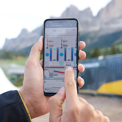 Hände halten Smartphone mit Polar mobile App zur Steuerung der SnowFactory vor Bergkulisse
