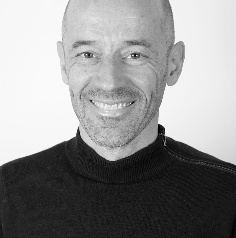 Nicolas Mabut, TechnoAlpin Mitarbeiter, Schwarz-Weiß-Portrait mit Glatze, breitem Lächeln und schwarzem Stehkragenpullover