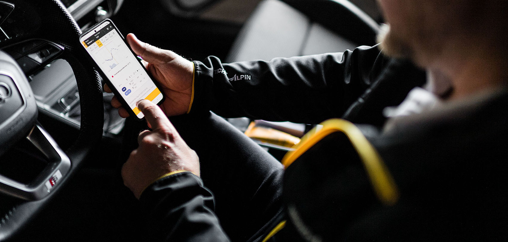 TechnoAlpin staff member in car reviewing Snowmaster app with snowmaking and weather data on smartphone