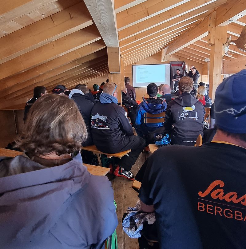 Teilnehmer einer Schulung in einem Holzraum verfolgen eine Präsentation auf einer Leinwand, Rückansicht des Publikums