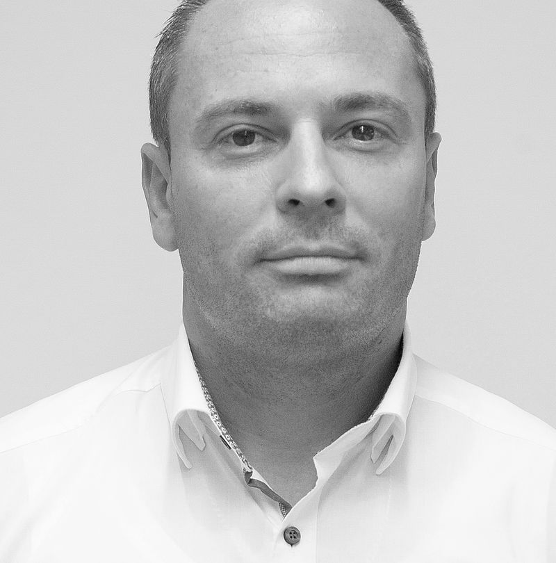 Christian Jocher, TechnoAlpin Mitarbeiter, Schwarz-Weiß-Portrait mit neutralem Lächeln, kurzem dunklem Haar und weißem Hemd