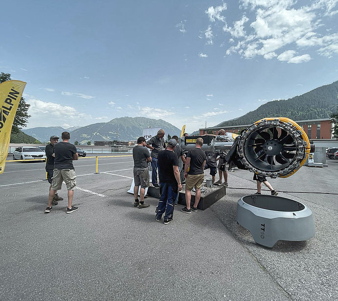 TechnoAlpin roadshow outdoors with TT10 snow generator and visitors in front of alpine panorama.