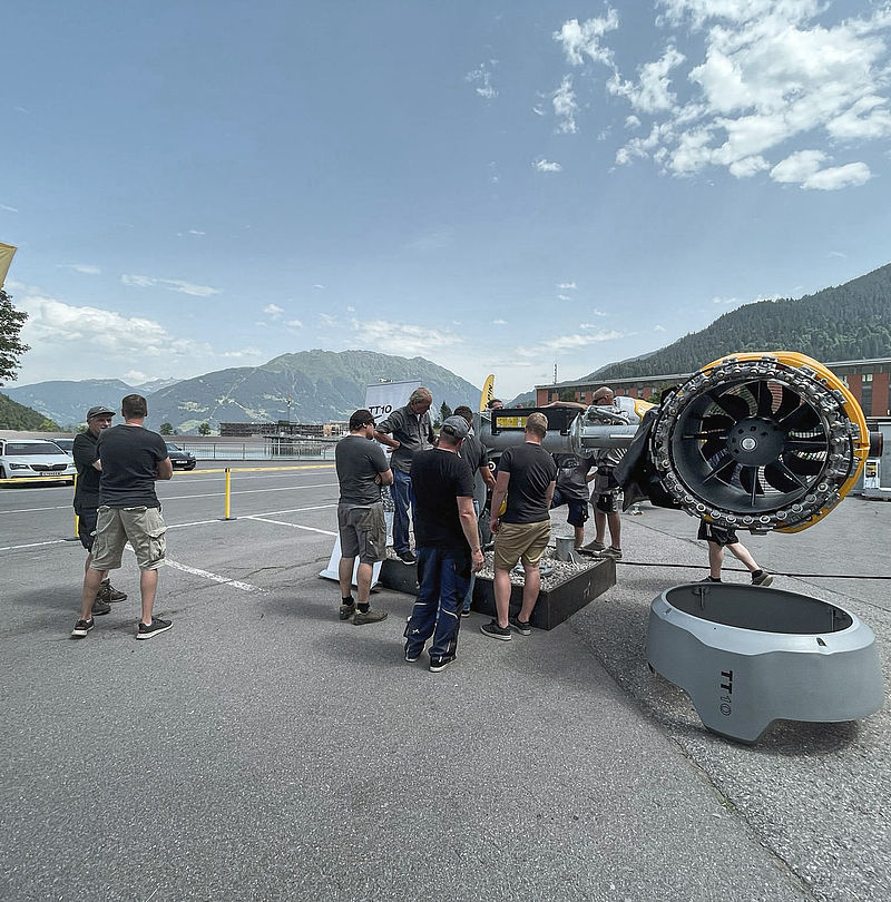 TechnoAlpin roadshow outdoors with TT10 snow generator and visitors in front of alpine panorama.