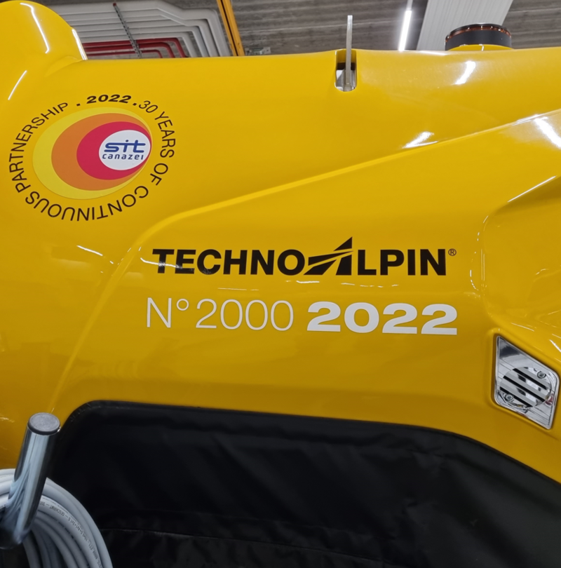 Gelber TechnoAlpin TR10 Schneeerzeuger mit Jubiläumslogo '30 Years of Continuous Partnership SIT Canazei N°2000 2022'