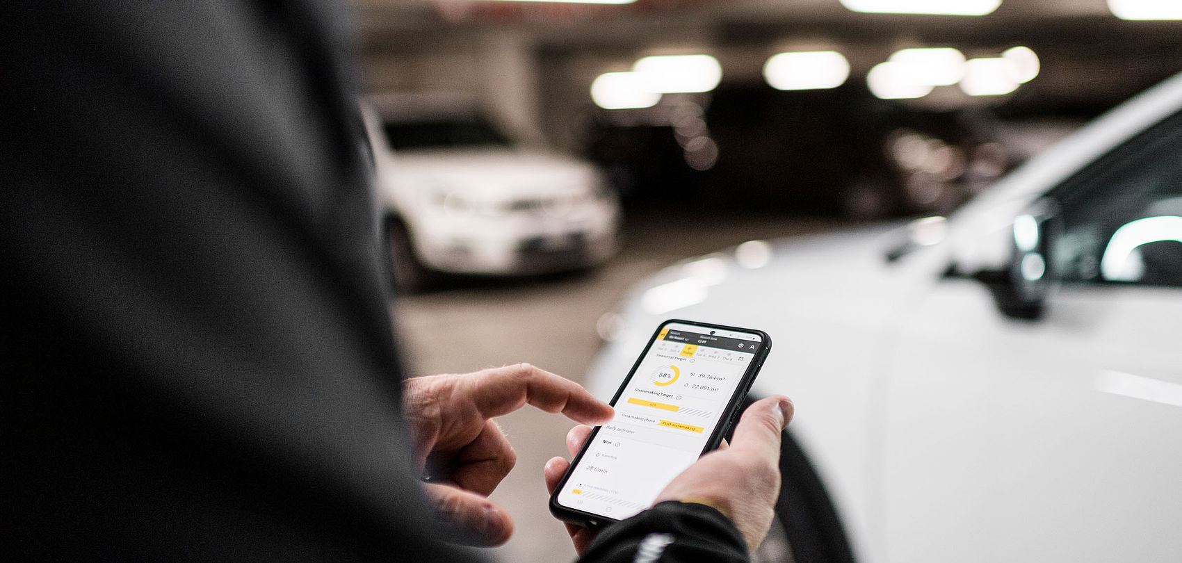 Personne utilisant l application mobile Snowmaster TechnoAlpin dans un parking pour surveiller l enneigement
