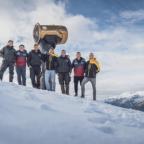 Sieben TechnoAlpin-Mitarbeiter feiern in Davos neben der goldenen Jubiläums-Schneekanone Nr. 1000 (2022) auf dem Berggipfel