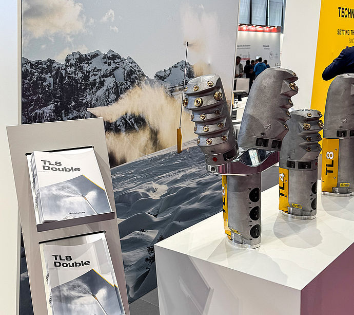 TechnoAlpin Messestand mit TL8 Double Broschüren und Schneeerzeuger-Düsenköpfen auf Podest