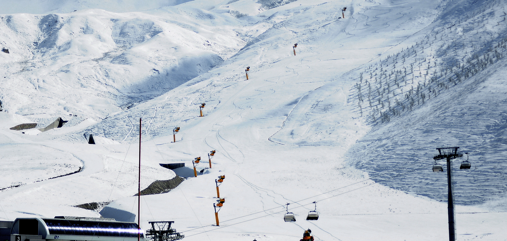 Rangée d'enneigeurs à hélice TechnoAlpin jaunes le long de la piste avec télésiège dans le domaine Shahdag