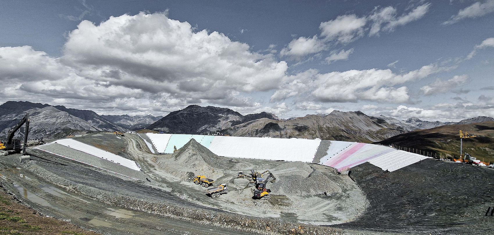 Baustelle Speicherteich mit weißer Folienabdeckung, Baggern und Bergpanorama