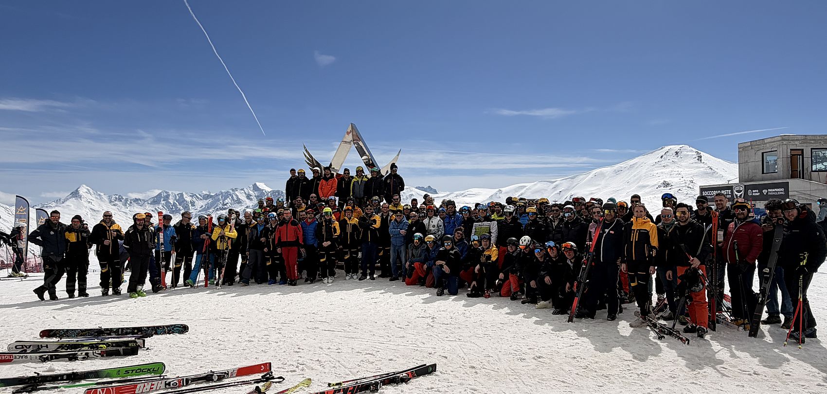 Große Gruppe von Skifahrern und Mitarbeitern posiert auf verschneiter Piste mit Skiern