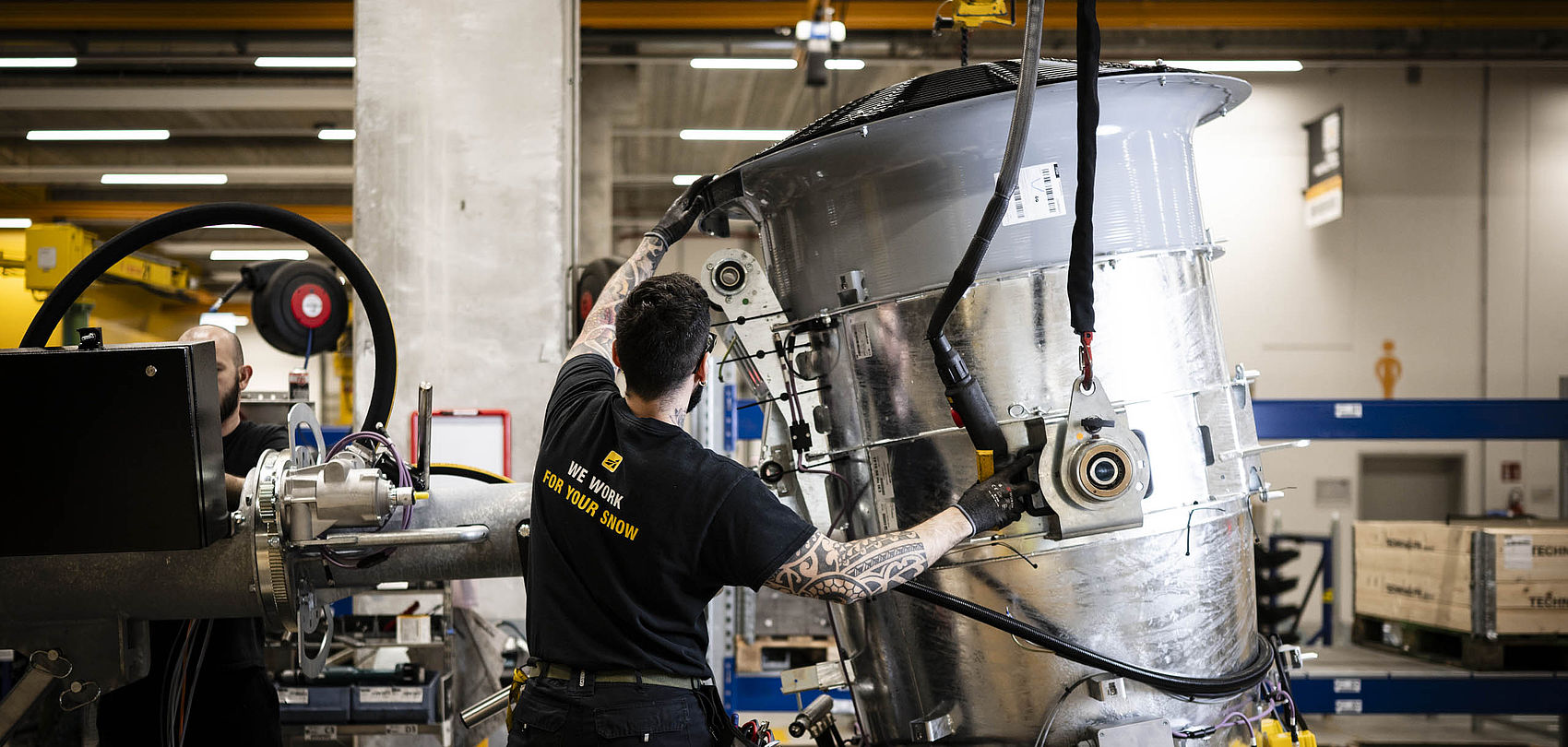 Techniker montiert großen zylindrischen Edelstahl-Schneeerzeuger an Kran in Produktionshalle