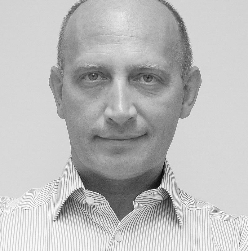 Sergej Ragosin, TechnoAlpin Mitarbeiter, Schwarz-Weiß-Portrait mit kurzem Haar, ruhigem Ausdruck und gestreiftem Hemd vor hellem Hintergrund