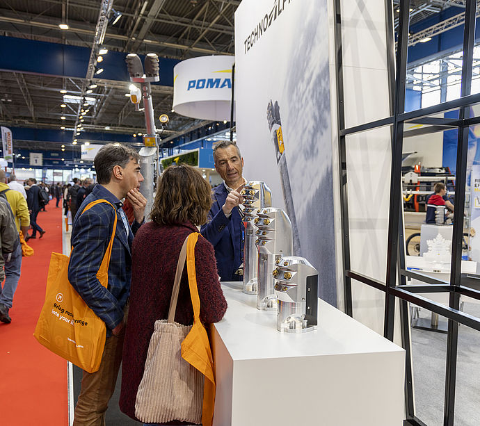 TechnoAlpin salesperson presenting nozzle head components to two visitors at stand.