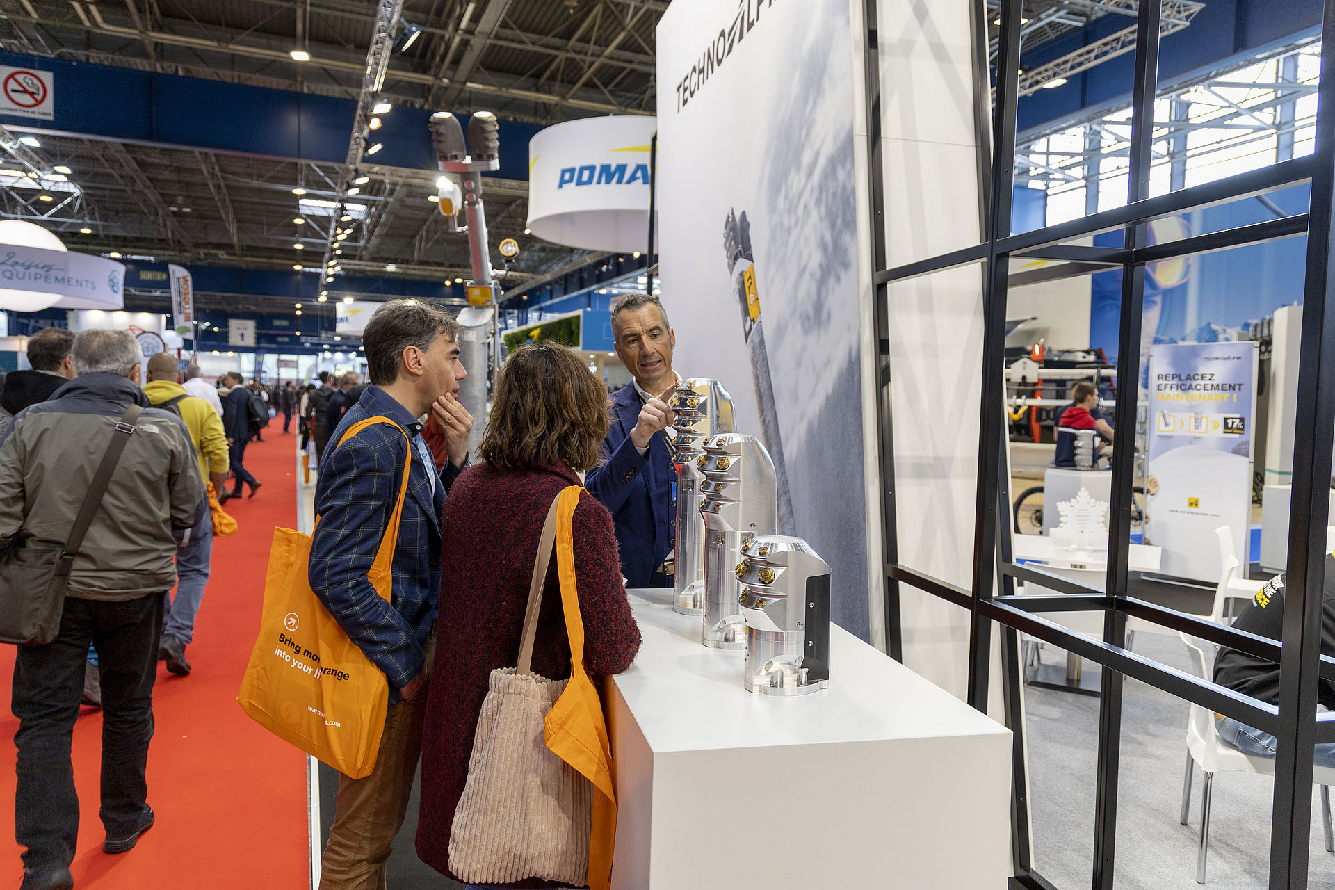TechnoAlpin salesperson presenting nozzle head components to two visitors at stand.