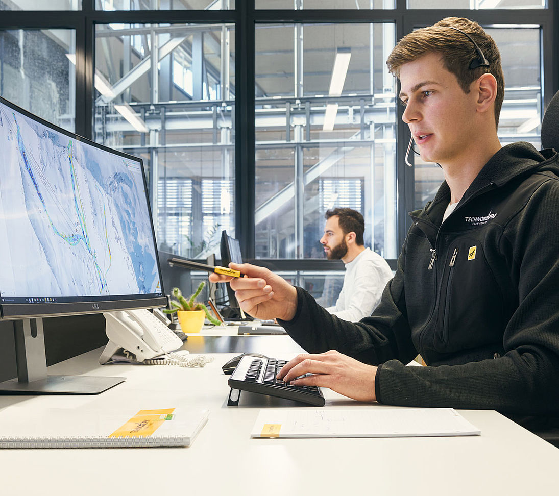 TechnoAlpin Techniker im Headset bei der Beratung mit Skigebietskarte am Bildschirm
