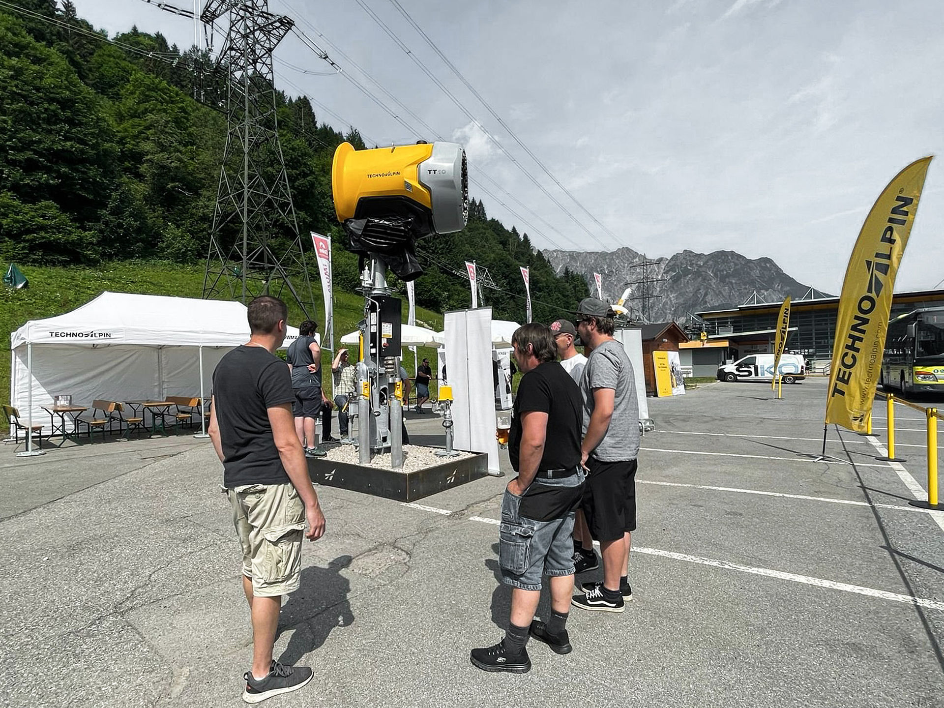 Visitors examining yellow TT10 snow gun on swivel arm at TechnoAlpin roadshow.