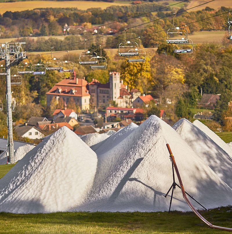Cumuli di neve bianca su prato verde con paesaggio autunnale, seggiovia e villaggio sullo sfondo
