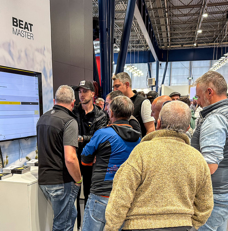 Messebesucher und Mitarbeiter im Gespräch am BEATmaster Bildschirm mit Steuerungssoftware
