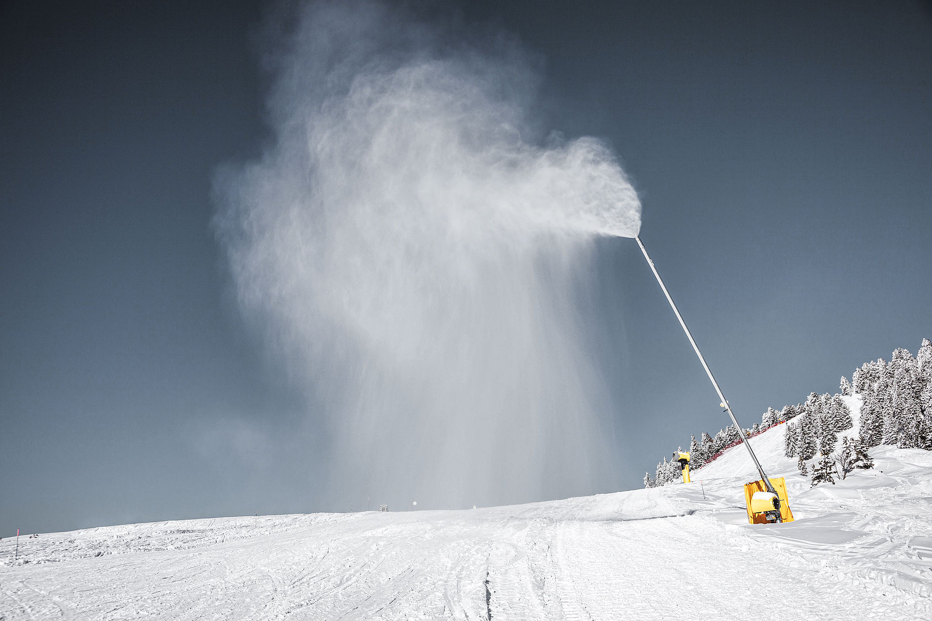 TechnoAlpin Schneilanze erzeugt Schnee auf einer Skipiste mit verschneiten Bäumen
