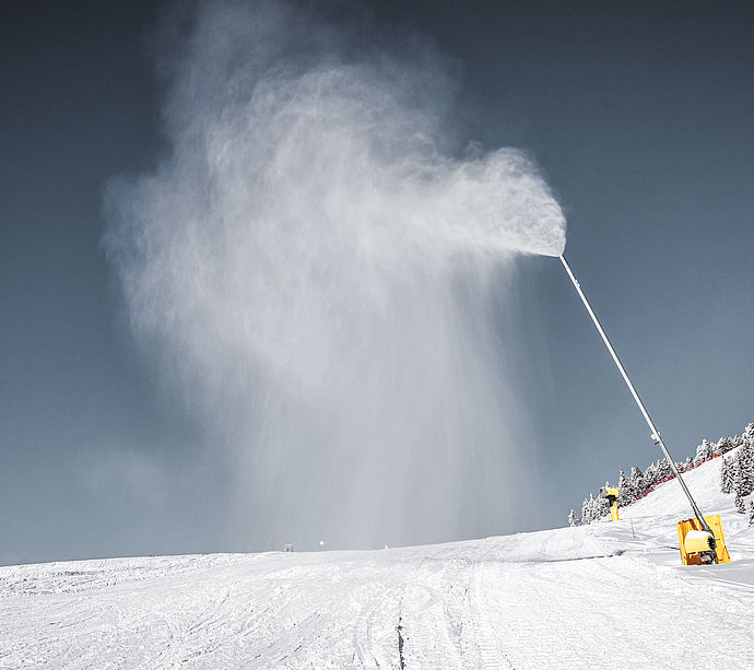 TechnoAlpin Schneilanze erzeugt Schnee auf einer Skipiste mit verschneiten Bäumen