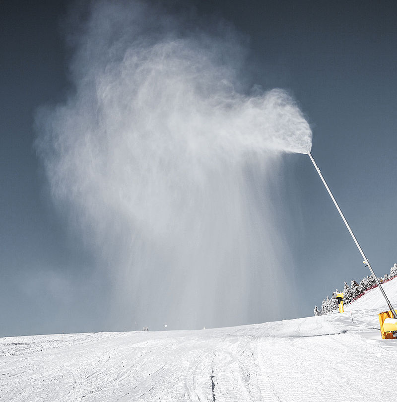 TechnoAlpin Schneilanze erzeugt Schnee auf einer Skipiste mit verschneiten Bäumen