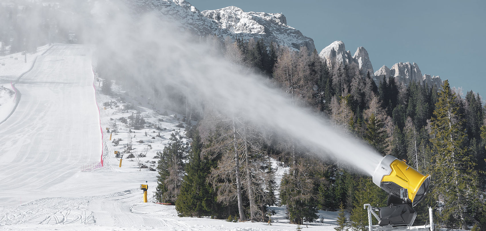 TR10 snow generator snowmaking on slope in front of mountain scenery with Dolomite peaks.