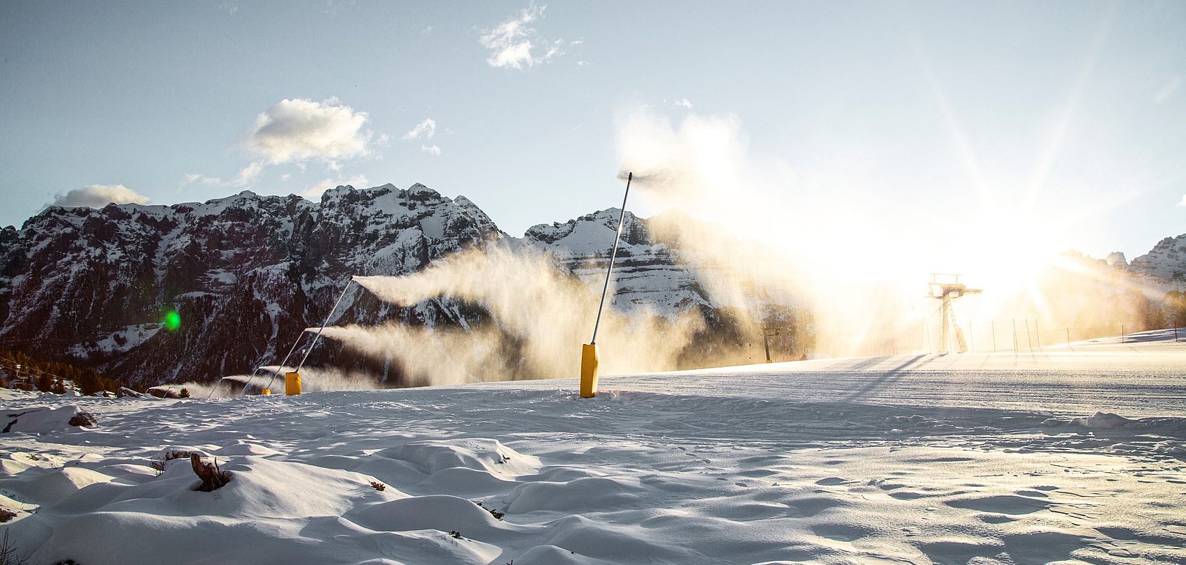Snow lance making snow on ski slope at sunrise with alpine panorama