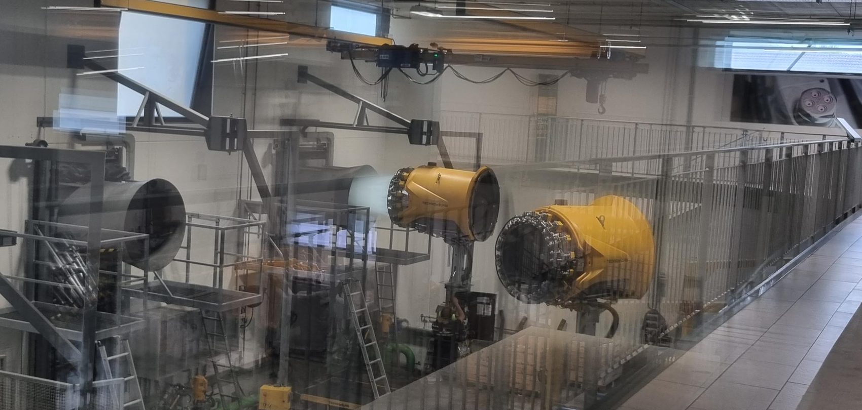 Blick durch Glasscheibe auf zwei gelbe Schneeerzeuger in industrieller Testanlage