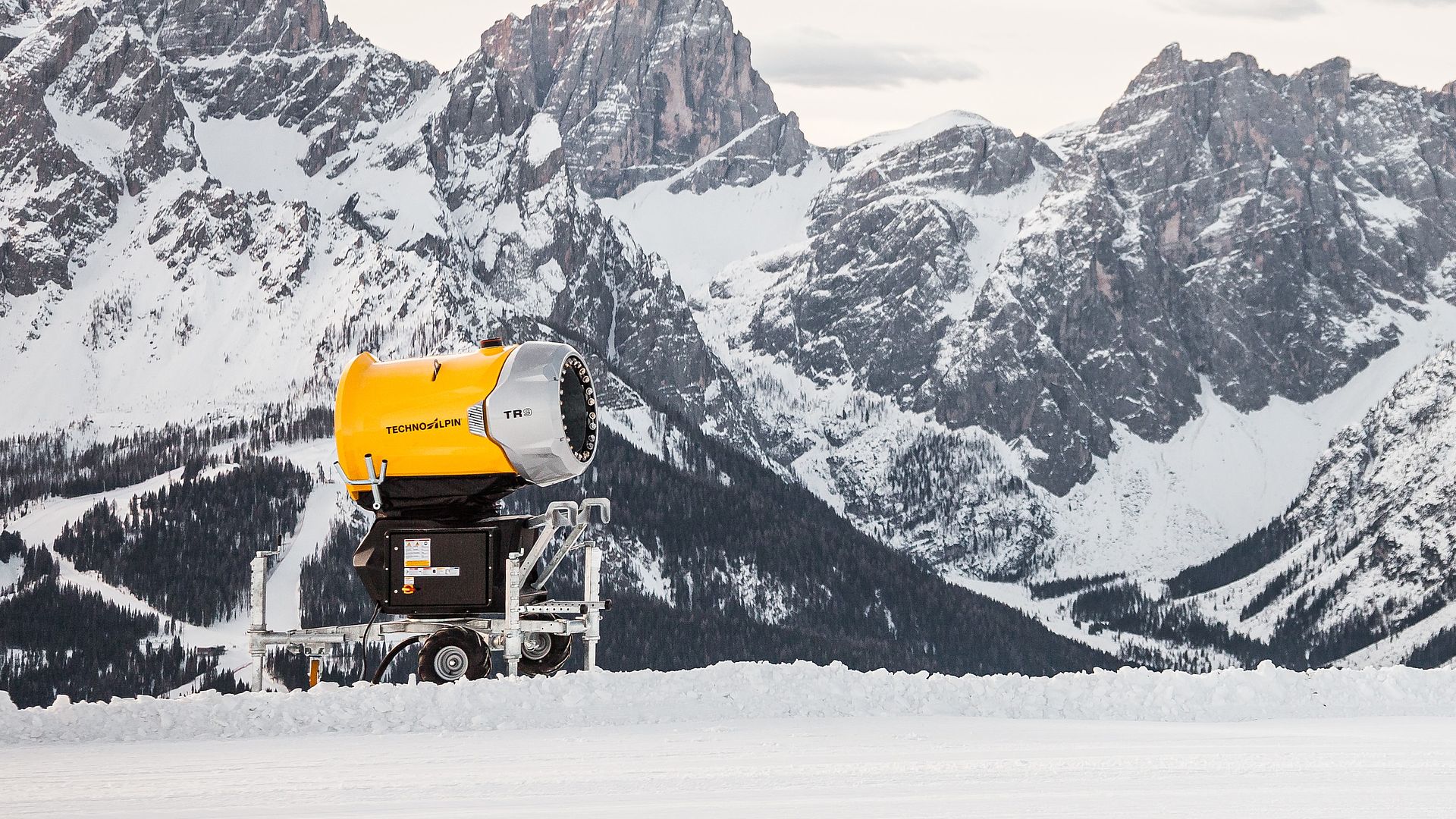 Gelbe TechnoAlpin TR9 Schneekanone vor verschneitem Dolomiten-Bergpanorama mit schroffen Felsgipfeln