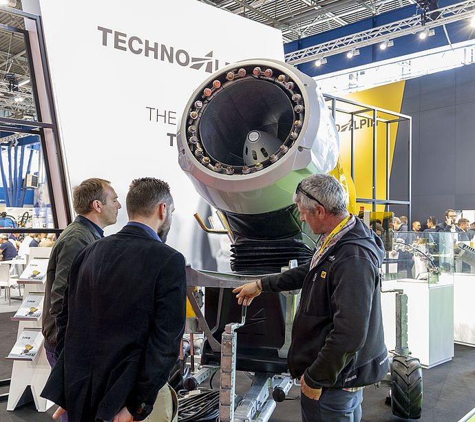 Three men examining open nozzle of large TechnoAlpin propeller machine.
