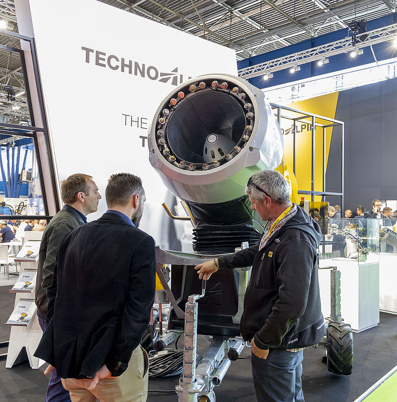 Three men examining open nozzle of large TechnoAlpin propeller machine.
