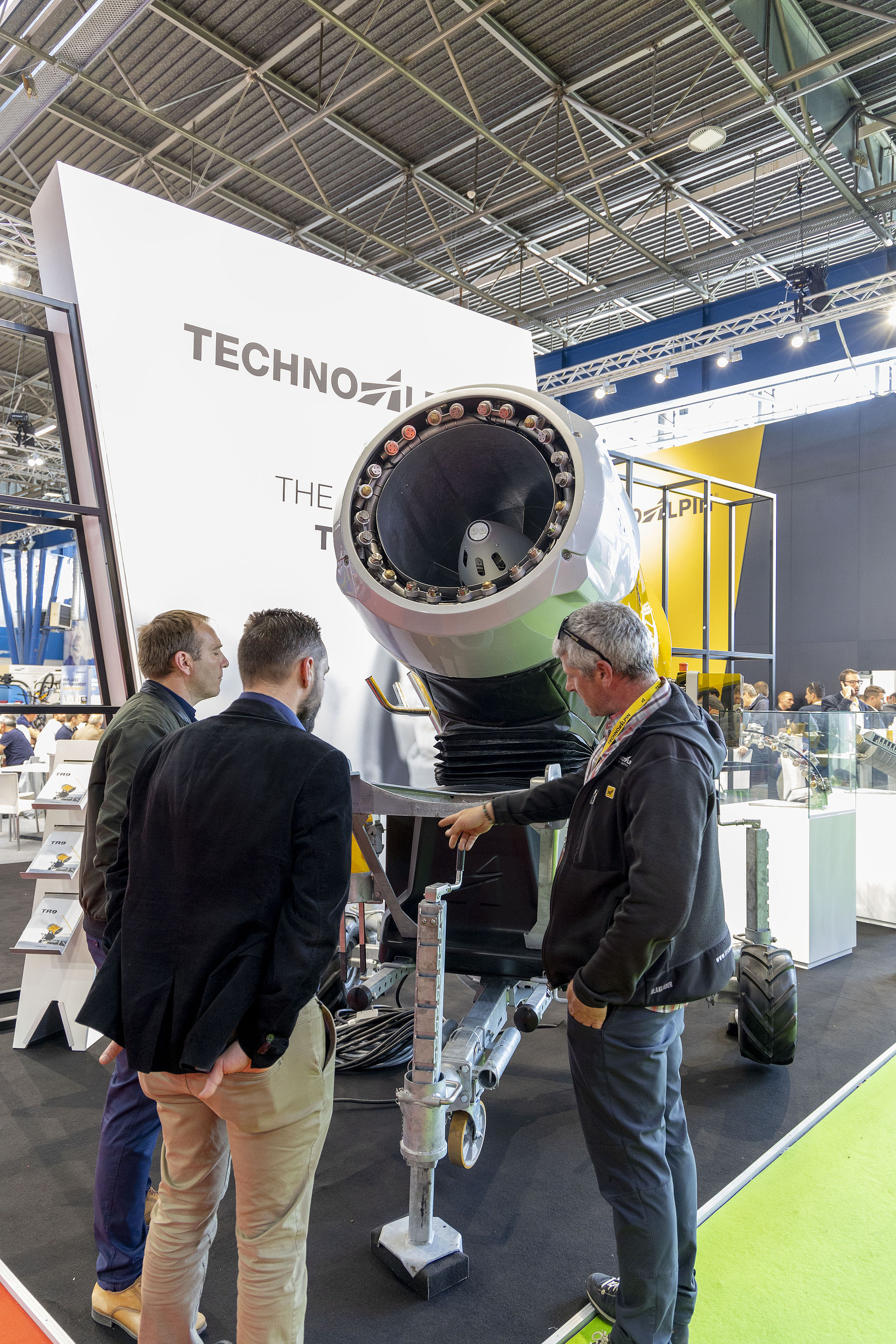 Three men examining open nozzle of large TechnoAlpin propeller machine.